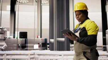 Mühendis fotovoltaik fabrikasında yürüyor, tabletteki sistem performans ölçümlerine bakıyor. İşçi sektörü 4.0 fabrika işletiyor, IoT sensörleri, kamera A aracılığıyla enerji üretimini takip etmek için aygıt kullanıyor.