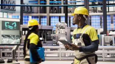 Akıllı fabrika teknisyeni donanımı değiştirmeden önce IoT sensörleri verilerini analiz etmek için tablet kullanıyor. Endüstri 4.0 'daki Afrikalı Amerikalı adam devre dışı kalma süresini azaltmak için sistem kontrolü yapıyor. Kamera A.