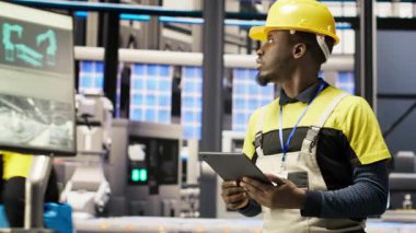 Akıllı fabrika teknisyeni donanımı değiştirmeden önce IoT sensörleri verilerini analiz etmek için tablet kullanıyor. Endüstrideki Afrikalı Amerikalı adam, 4.0 bitki sistemi sistem kontrolü yapıyor, dinlenme süresini azaltmak için, kamera B
