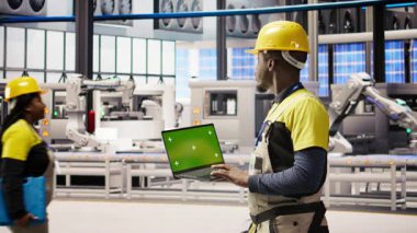 Güneş panelleri fabrika mühendisi vites arızalarını tahmin etmek için performans verilerini yeşil ekran laptopuyla analiz ediyor. Fotovoltaik fabrika işçisi bakım prosedürlerini takip etmek için maket defteri kullanır, kamera A