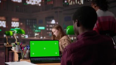 Üniversite kampüs kütüphanesinde yeşil ekranla çalışan genç öğrenci, doğrulanmış eğitim kaynaklarından akademik bilgi topluyor. Öğrenci araştırma araçlarını kullanıyor. Kamera B.