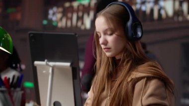 Dizüstü bilgisayarla ilgili eğitici belgesel dinleyen ve notlar alan genç bir kız, üniversite kütüphanesinin sessizliğinde ders çalışmak için geleneksel olmayan modern yöntemleri kullanıyor. Akademik veri topluyor. Kamera A.