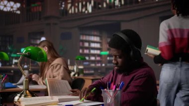 Ortam müziği dinleyen, kulaklıkla müzik dinleyen ve okul projelerine odaklanan bir kitaptan veri toplayan erkek öğrenci. Okul ödevini bitirmek için ortam müziğinin tadını çıkarıyorum. Kamera B.