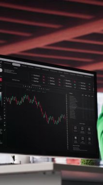 Dikey Video Afrikalı Amerikalı adam hisse senedi almak ve satmak için PC kullanıyor. Forx grafiklerini ve diyagramlarını izliyor. Borsada çalışan bir borsa simsarı bilgisayardaki mum çubuğu çizelgelerine bakıyor. Kamera A.