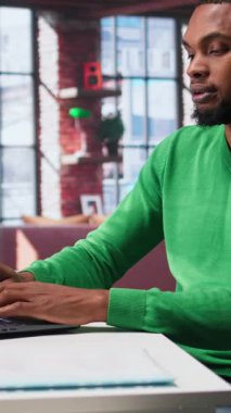 Evdeki Dikey Video Adam, yanlış duruş nedeniyle rahatsız olan sandalyeye bağlı olarak sırt ağrısı ve esneme eklemleriyle ilgilenir. Siyahi adam çok çalışıyor ve masada kas krampları yaşıyor.