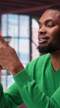 Sosyal medya paylaşımları yazmak için akıllı telefonu kullanarak evde dikey videocu, serbest çalışan olarak içerik üretiyor. Afrikalı Amerikalı adam cep telefonuyla profil takibi yapıyor. Kamera A.