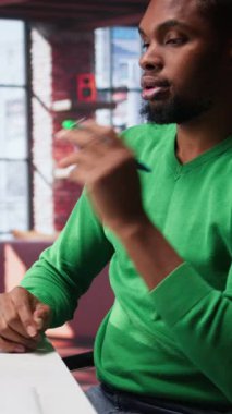 Dikey Video Black serbest çalışanı kâr ve ulaşımı arttırmak için yeni çözümler düşünüyor, finansal büyüme için fikirler bulmak için birden fazla iş yapıyor. Genç uzaktan kumandalı işçi, yaratıcılığını başarı için kullanır. Kamera.