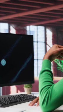 Vertical Video Teleworker merkez ofiste PC 'deki iş konferansını izliyor, istatistik tablolarına bakıyor. Apartmandaki Afrikalı Amerikalı uzaktan çalışan bilgisayardaki sunum grafiklerine bakıyor.