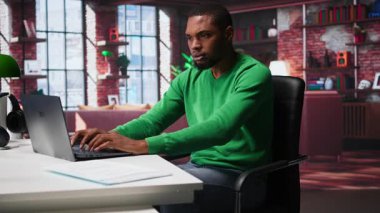 Uzaktan kumandalı çalışan siyahi bir adam masasında huzursuz ve endişeli bir şekilde bacaklarını sallıyor ve görev bitimi ve teslim tarihi nedeniyle gergin. Baskı ve endişe altında çalışan serbest çalışan biri. Kamera B.