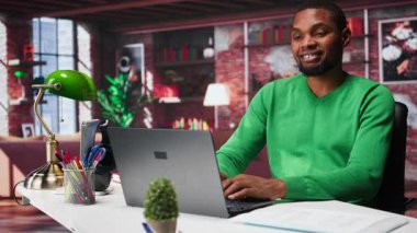 Web atamaları için dizüstü bilgisayar kullanan, sunum slaytları hazırlayan ve veri planları üzerinde çalışan siyah bir çalışan. Genç tele-işçi şirket projesini bitiriyor. Kamera B.