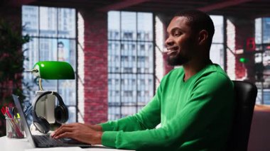 Afrikalı Amerikalı uzaktan kumandalı işçi evde online araştırma yapıyor, önemli verileri yazıyor ve topluyor. Teleworker, evdeki günlük ödev ve makaleleri okumaya odaklandı. Kamera A.