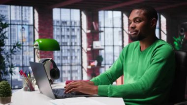 Afrikalı Amerikalı uzaktan kumandalı işçi evde online araştırma yapıyor, önemli verileri yazıyor ve topluyor. Teleworker, evdeki günlük ödev ve makaleleri okumaya odaklandı. Kamera B.