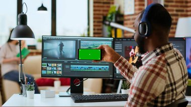 Erkek film yapımcısı, bir video projesini fotokopi ekranı kullanarak modern bir renk derecelendirme yazılımında düzenliyor. Genç adam video yapımının yaratıcı sürecinde çift monitörlerde çalışıyor. Kamera B.