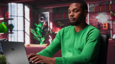 Afrika kökenli Amerikalı uzaktan kumandalı işçi günlük iş ödevlerini çözüyor, modern çatı katının rahatlığıyla işlerini online olarak bitiriyor. İnternete bağlanmış genç bir tele-işçi, birden fazla iş yapıyor. Kamera A.