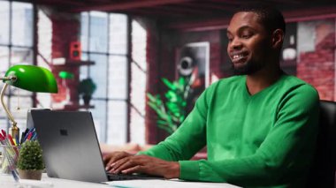 Web atamaları için dizüstü bilgisayar kullanan, sunum slaytları hazırlayan ve veri planları üzerinde çalışan siyah bir çalışan. Genç tele-işçi şirket projesini bitiriyor. Kamera A.