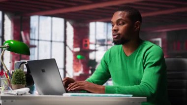 Modern bir stüdyo dairesindeki dizüstü bilgisayarda web 'e odaklanmış erkek serbest çalışan, sanal bir çalışma alanında bağımsızlık, bağlantı ve üretkenlik yaşam tarzını gösteriyor. Adam birden fazla iş yapıyor. Kamera A.