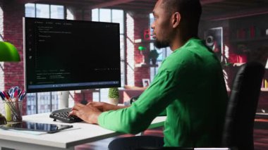 Merkez ofisteki siyah teknisyen UI 'ye bilgisayar monitöründe bakar, programlama kodunu yazar ve çalıştırır. Modern dairede kodlama uygulaması kullanarak kod yazıp test eden bilişim işçisi. Kamera B.