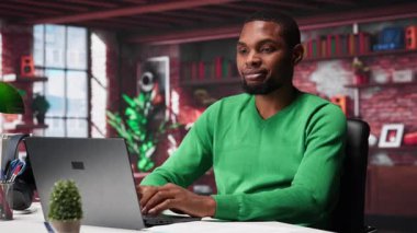 Evdeki siyah tele-sekreter belgeleri düzenlemek ve günlük görevleri çözmek için dizüstü bilgisayar açıyor, raporları ve dosyaları güncelliyor. Uzaktan kumandalı ve dijital evrak işleriyle uğraşan genç bir çalışan. Kamera A.