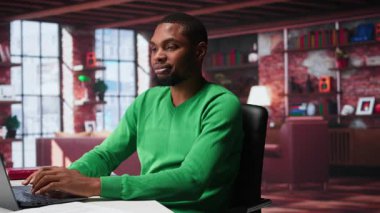 Evdeki siyah tele-sekreter belgeleri düzenlemek ve günlük görevleri çözmek için dizüstü bilgisayar açıyor, raporları ve dosyaları güncelliyor. Uzaktan kumandalı ve dijital evrak işleriyle uğraşan genç bir çalışan. Kamera B.