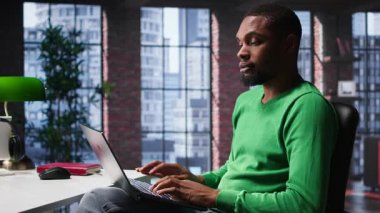 Afrika kökenli Amerikalı uzaktan kumandalı işçi günlük iş ödevlerini çözüyor, modern çatı katının rahatlığıyla işlerini online olarak bitiriyor. İnternete bağlanmış genç bir tele-işçi, birden fazla iş yapıyor. Kamera B.