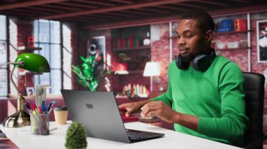 Modern çatı katındaki masasına kişisel notlar yazan Afrika kökenli Amerikalı erkek tele-işçi. Evde oturan üretken adam ders kitabına not almak için kalem kullanıyor. Kamera B.