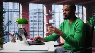 Çatı katındaki bilgisayarında yazı yazan Afro-Amerikan bir yetişkin. Çevrimiçi serbest çalışma ve verimli bir şekilde birçok iş yapıyor. Rahat bir ofiste uzaktan kumandanın esnekliği. Kamera B.