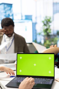 CEO, iş ortaklarıyla yaptığı toplantıda proje geliştirme sürecini gözden geçirmek için yeşil ekranlı dizüstü bilgisayar kullanıyor. Stratejik hedefleri sağlamak için detaylı analiz ve modellemeler kullanılıyor.
