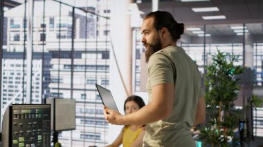 Neşeli yönetici elinde bilgisayarla iş arkadaşlarıyla sohbet ederken aynı zamanda makine öğrenme teknolojisi ile çalışıyor. Adam not defteri kullanarak verileri tahmin edilebilir modellere dönüştürüyor ve iş arkadaşlarıyla konuşuyor, kamera A