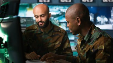 Hava kuvvetleri subayı ve iş arkadaşı komuta merkezinde taktik seviyesinde gözetleme yaparken konuşuyor. Saldırı bölgelerine ve kamera A 'ya bakmak için radar ekipmanı kullanan askeri ekip çalışanları.