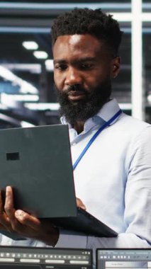 Dikey video Happy veri merkezi yöneticisi dizüstü bilgisayarda düğüm ağacı programlama kullanıyor, iş arkadaşıyla beşlik çakıyor. Gülümseyen sunucu tarla işçisi iş arkadaşını selamlıyor, veri analiz grafiğini inceliyor, kamera B