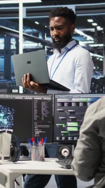 Dikey video Happy veri merkezi yöneticisi dizüstü bilgisayarda düğüm ağacı programlama kullanıyor, iş arkadaşıyla beşlik çakıyor. Gülümseyen sunucu çiftliği çalışanı iş arkadaşını selamlıyor, veri analiz grafiğini inceliyor, kamera A