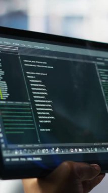 Veritabanı yazılım geliştiricisinin donanımı güncellemek için kullanılan tablet üzerindeki kodları kontrol ettiği dikey video. Sunucu merkezi uzmanı, aygıt üzerinde programlama dili betiği kullanarak bakım, kamera B