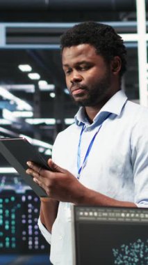 Dikey Veri Merkezi teknisyeni tablet kullanarak düğüm ağacı programlama ve kaynak tahsisini optimize ediyor. Sunucu odası bilişim uzmanı bakım planlama için öngörücü yapay zeka görselleştirme sistemleri kullanıyor