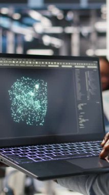 Yapay zeka veri analizi grafiklerini yorumlamak için laptop kullanan veri merkezi çalışanının dikey videosu. Sunucu odası teknisyeni, sistem ölçümlerinde yapay zeka kullanıyor.