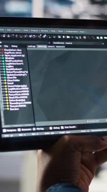 Veritabanı yazılım geliştiricisinin donanımı güncellemek için kullanılan tablet üzerindeki kodları kontrol ettiği dikey video. Sunucu merkezi uzmanı, aygıt üzerinde programlama dili betiği kullanarak bakım, kamera A