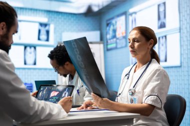 Özel bir klinikte x ışını analizi üzerinde işbirliği yapan tıp uzmanları, kesin tanı ve etkili tedavi planları sağlayan kolektif çalışmalar. Profesyonel sağlık hizmetleri ekip çalışmasının vurgulanması.