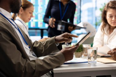 Tablet üzerindeki bilgi grafikleri ve kaynak tahsisini inceleyen hissedar, strateji oturumu için ortaklarla bir araya geliyor. Büyüme için yenilikçi çözümler geliştirmek için veri analizlerinin kullanılması.