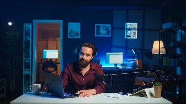 Stüdyodaki nüfuzlu kişi marka sponsorluk videosundan dizüstü bilgisayarı onaylıyor, mikrofonla konuşuyor. İçerik yaratıcı, yüksek teknolojili mikrofon ve kamera B ile kayıt yaparak pazarlamayı etkiler.