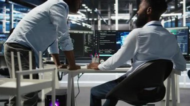 Sunucu merkezi yöneticisi yapay zeka veri analizi grafiklerini kontrol ediyor, çalışanı tebrik ediyor. Veri merkezi ekip lideri, yapay zeka kullanarak yöneticisiyle yumruk tokuşturuyor. Sistem ölçümlerini, kamera A 'yı gösteriyor.