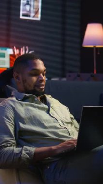 Dikey Video Analisti, ürün ve hizmetler hakkında stratejik tavsiyelerde bulunmak için aylık bütçeyi ve giderleri inceliyor. Zenci genç iş adamı gelir dengesi analizi yapıyor, evde muhasebe yapıyor. Kamera A.