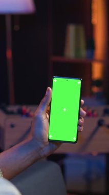 Dikey Video Afrikalı Amerikalı genç yetişkin kanepede yatıyordu, evde esnek çalışma saatleriyle mutlu ve rahat hissediyordu. Freelancer oturma odasında telefonu dinlendirici olarak kullanıyor.