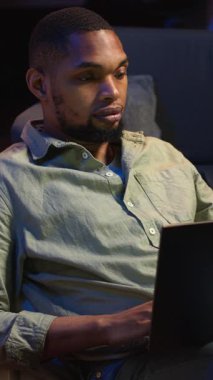 Dikey Video Analisti, ürün ve hizmetler hakkında stratejik tavsiyelerde bulunmak için aylık bütçeyi ve giderleri inceliyor. Zenci genç iş adamı gelir dengesi analizi yapıyor, evde muhasebe yapıyor. Kamera B.