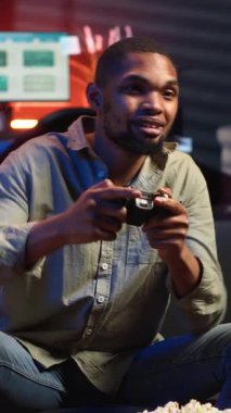 Dikey Video POV genç siyahi yetişkin akıllı TV 'de atış oyunu oynayarak, oturma odasında konsol takarak ve geceleri oyun oynayarak eğleniyor. Eğlenceli aktiviteler yapan bir adam. Kamera.