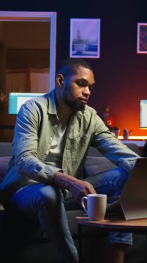 Dikey Afrikalı Amerikalı, oturma odasındaki kablosuz bilgisayarında internete bağlanıp serbest çalışmayla evde dinleniyor. Adam günlük işleri bitirmek için birden fazla iş yapıyor.