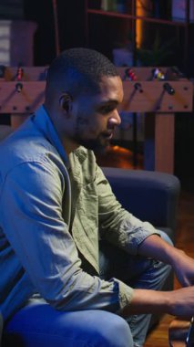 Dikey Video Genç Siyah Yetişkin, oturma odasında kendi başına çalışıyor, iş programını ayarlıyor ve rahat evinden işten keyif alıyor. İnternette dizüstü bilgisayarla gezinen kişi, çoklu görev