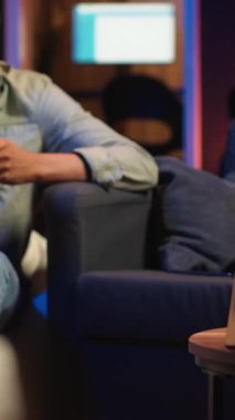 Dikey Video Siyah uzaktan kumandalı işçi ekranın yanında geziniyor, analitik çalışıyor, evde oturuyor ve birden fazla aygıtla günlük görevleri üzerinde çalışıyor. Çatı katında boş zaman ve iş verimliliği. Kamera.