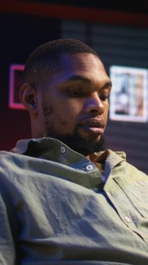 Dikey video odaklı siyahi kişi, şık çatı katında dizüstü bilgisayarda birden fazla iş yapar, internete bağlanır ve günlük serbest işleri ve uzak sorumlulukları yönetir. Kanepede ağ taraması