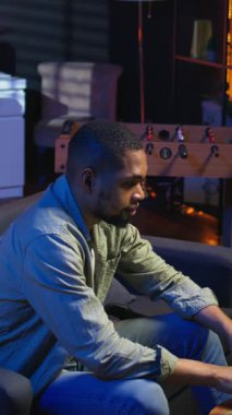 Dikey Video Afrikalı Amerikalı Serbest Çalışan, oturma odasındaki kanepede otururken kulaklık kullanarak internet üzerinden yapılan bir yayını dinliyor. Sıradan bir evde birden fazla iş. Kamera A.