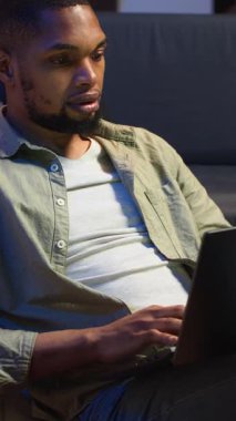 Dikey Afrikalı Amerikalı sıradan bir adam evdeki bilgisayarında günlük görevleri çözüyor, uzaktan kumandalı serbest iş yapıyor. Genç yetişkin internette sörf yapıyor ve rahat bir dairede birden fazla iş yapıyor.