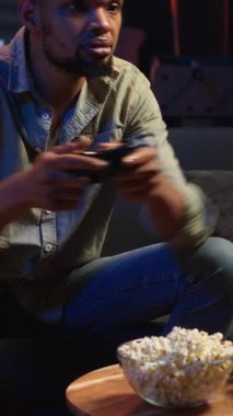 Evde boş zamanlarında video oyunlarıyla eğlenen, çevrimiçi atış turnuvasındayken patlamış mısır yiyen dikey video oyuncusu. Gevşemiş adam atıştırmalıklar ve yarışmayla oyun gecesinin tadını çıkarıyor.